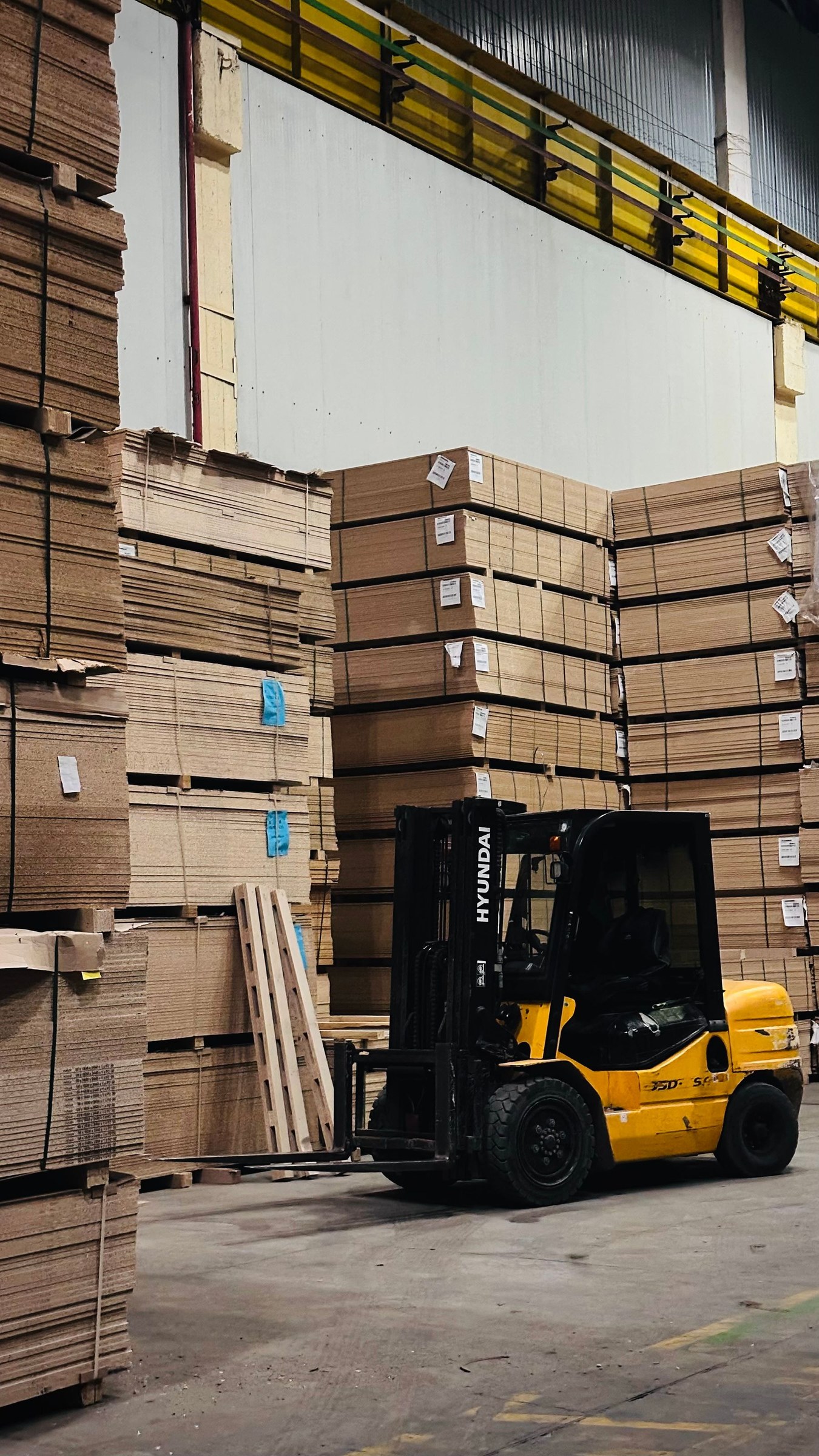 Yellow forklift parked beside stacks of flat cardboard sheets in a warehouse