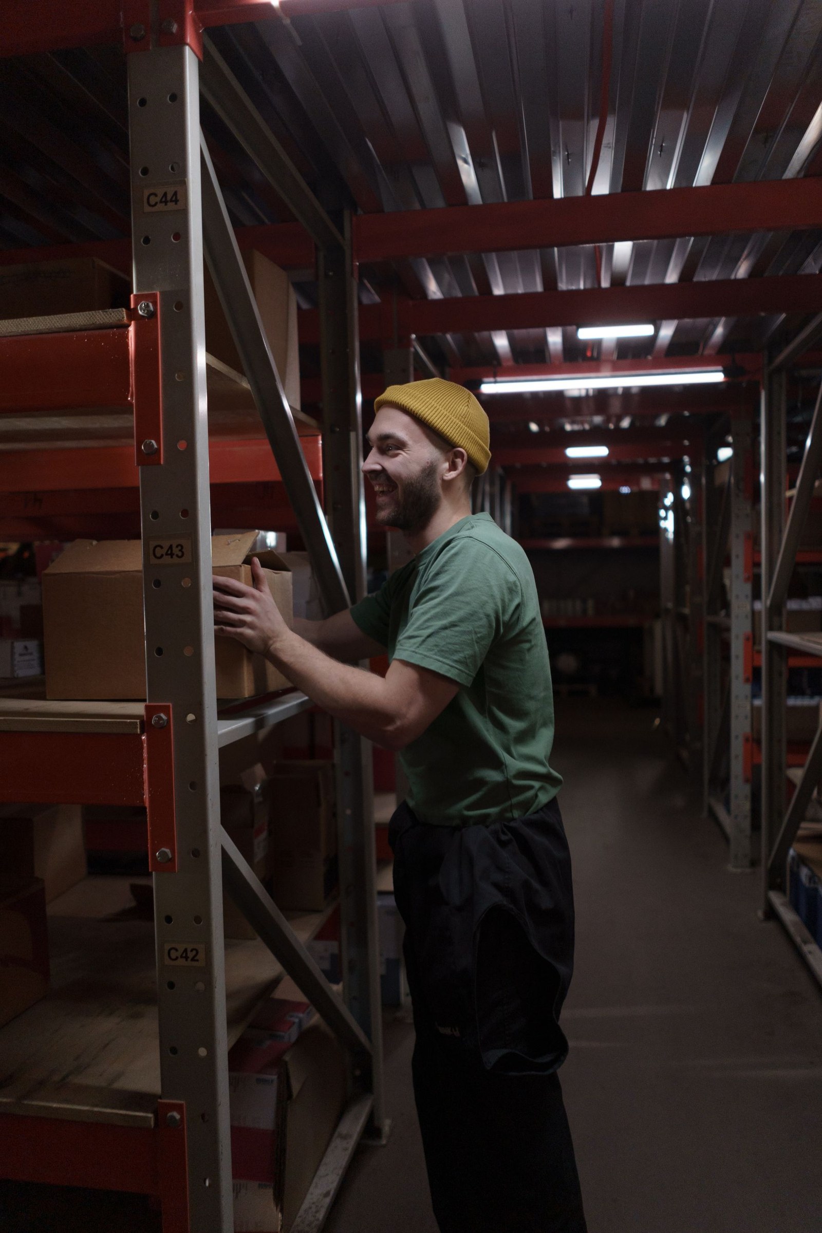 Warehouse worker in a green shirt placing a cardboard box on storage shelves